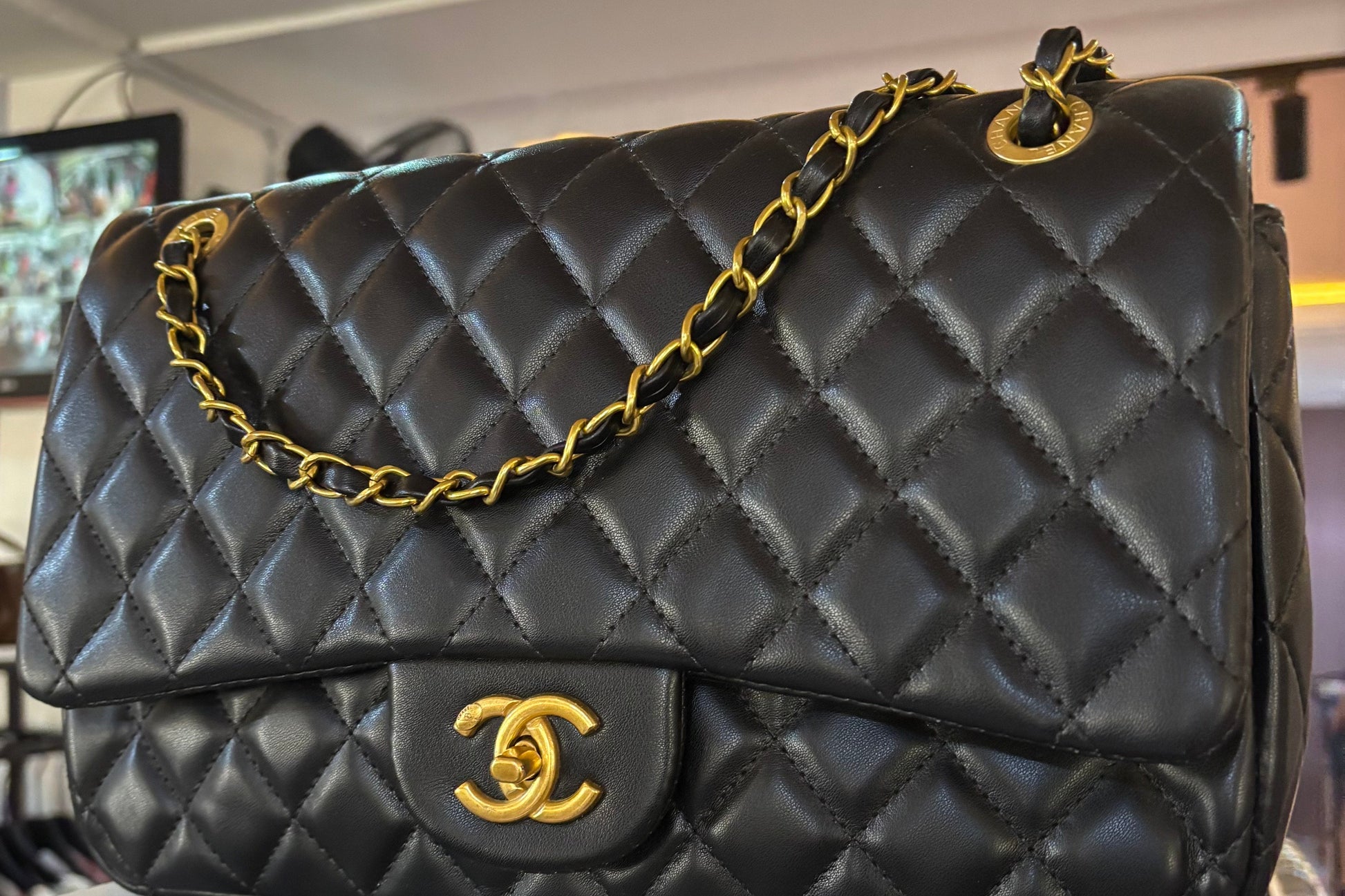 Black quilted handbag with gold chain and clasp on a blurred indoor background